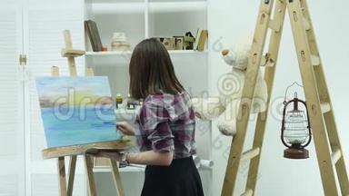 一位年轻女子站在画架后面的一张画布上，在一个<strong>大气</strong>车间里画一幅画